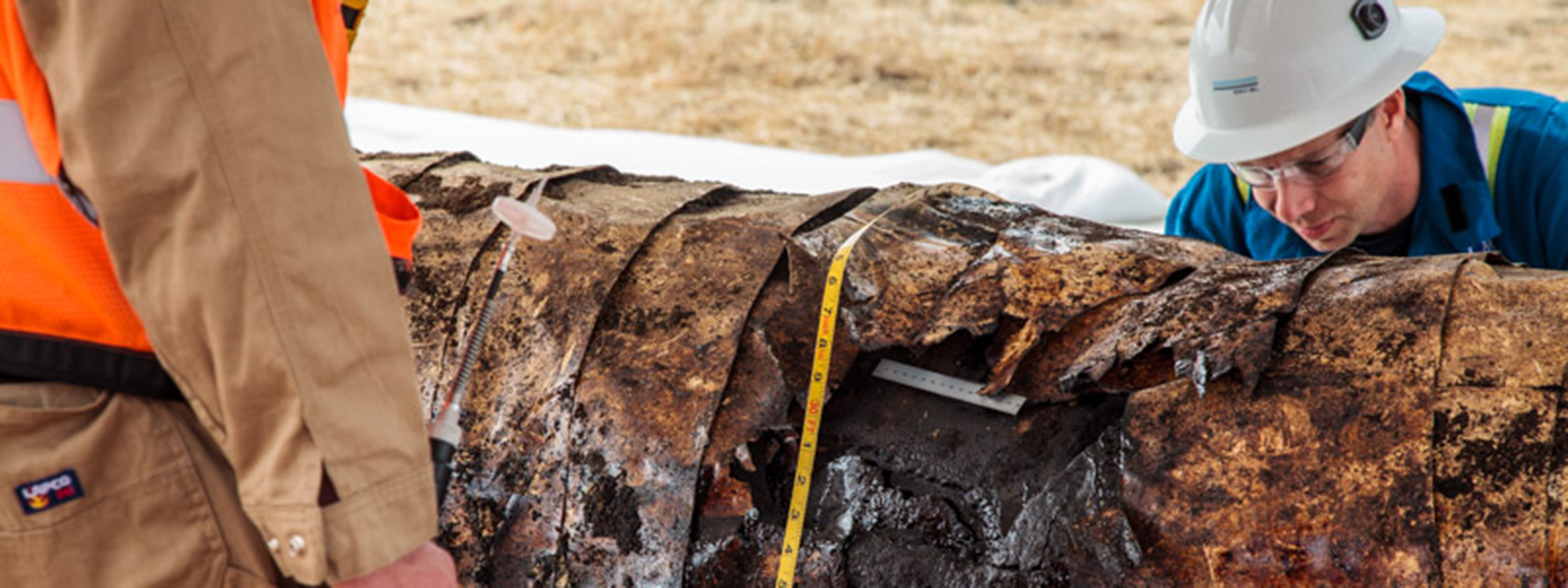 rusty oil pipeline with individuals inspecting it